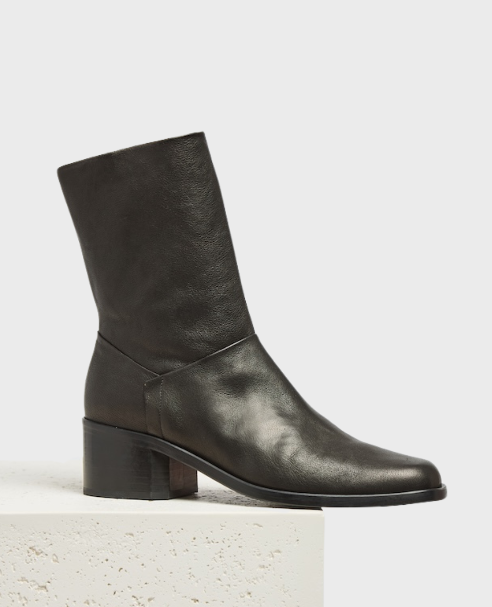 A sleek, black leather ankle boot with a mid-height block heel, smooth texture, and a square toe, featuring a minimalist design with no visible laces or zippers.