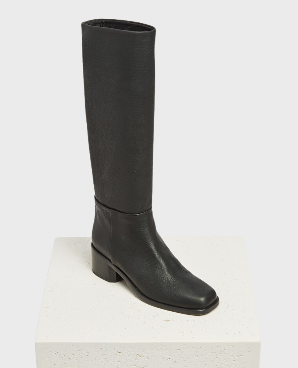 A tall, black leather boot with a smooth texture, a rounded square toe, a to-the-knee-calf height, and a low, chunky heel.