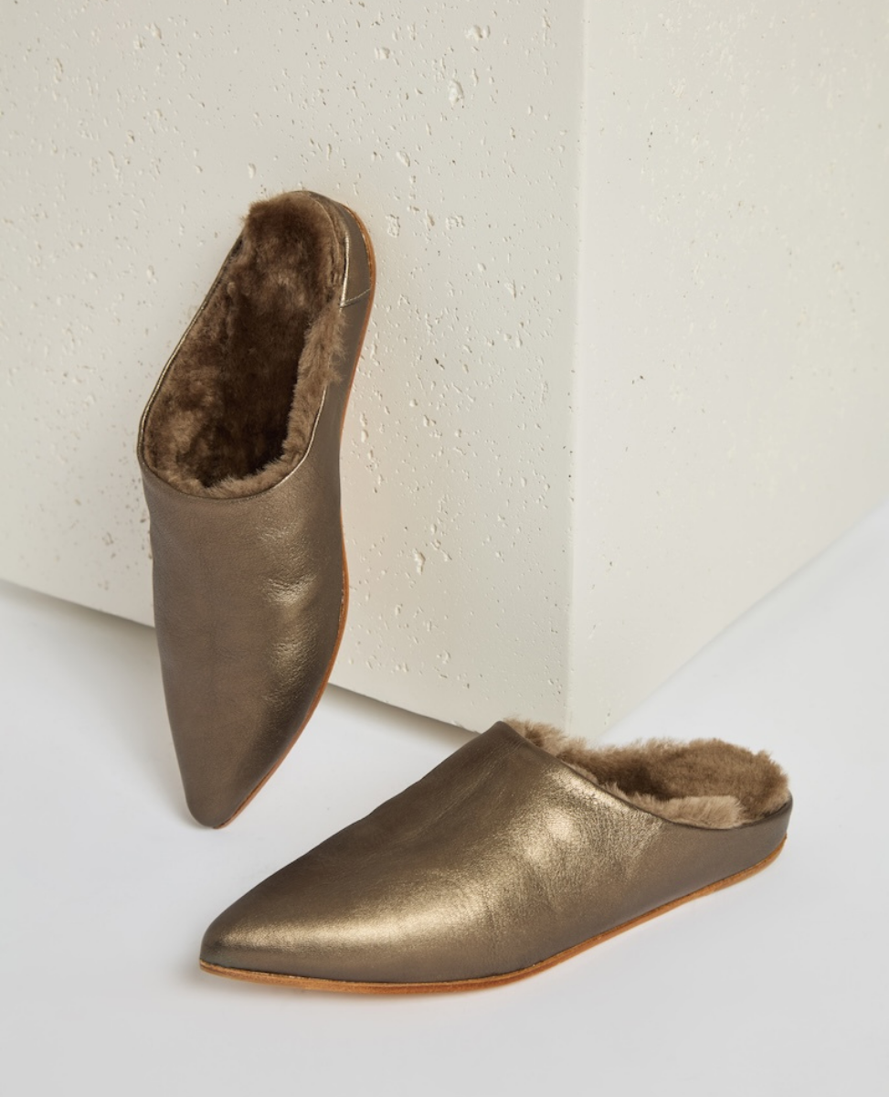 A pair of metallic bronze, pointed-toe slippers with a soft, plush brown interior lining and a smooth, slightly textured exterior, featuring a flat sole and a slip-on design.